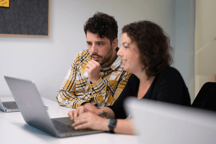 Zwei Personen sitzen vor einem Laptop.